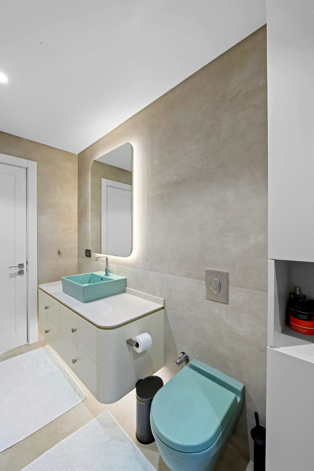 Bu modern lüks villa banyosunda, bej tonlarındaki büyük ebatlı seramik kaplamalar mekâna sade ve zarif bir temel oluşturuyor. Nötr renklere canlılık katan pastel su yeşili lavabo ve klozet takımı, yuvarlak hatlı yüzer dolap tasarımıyla birlikte dikkat çekici bir detay sunuyor. Arkadan aydınlatmalı aynanın yaydığı yumuşak ışık, mekânın temiz, aydınlık ve ferah atmosferini vurguluyor.