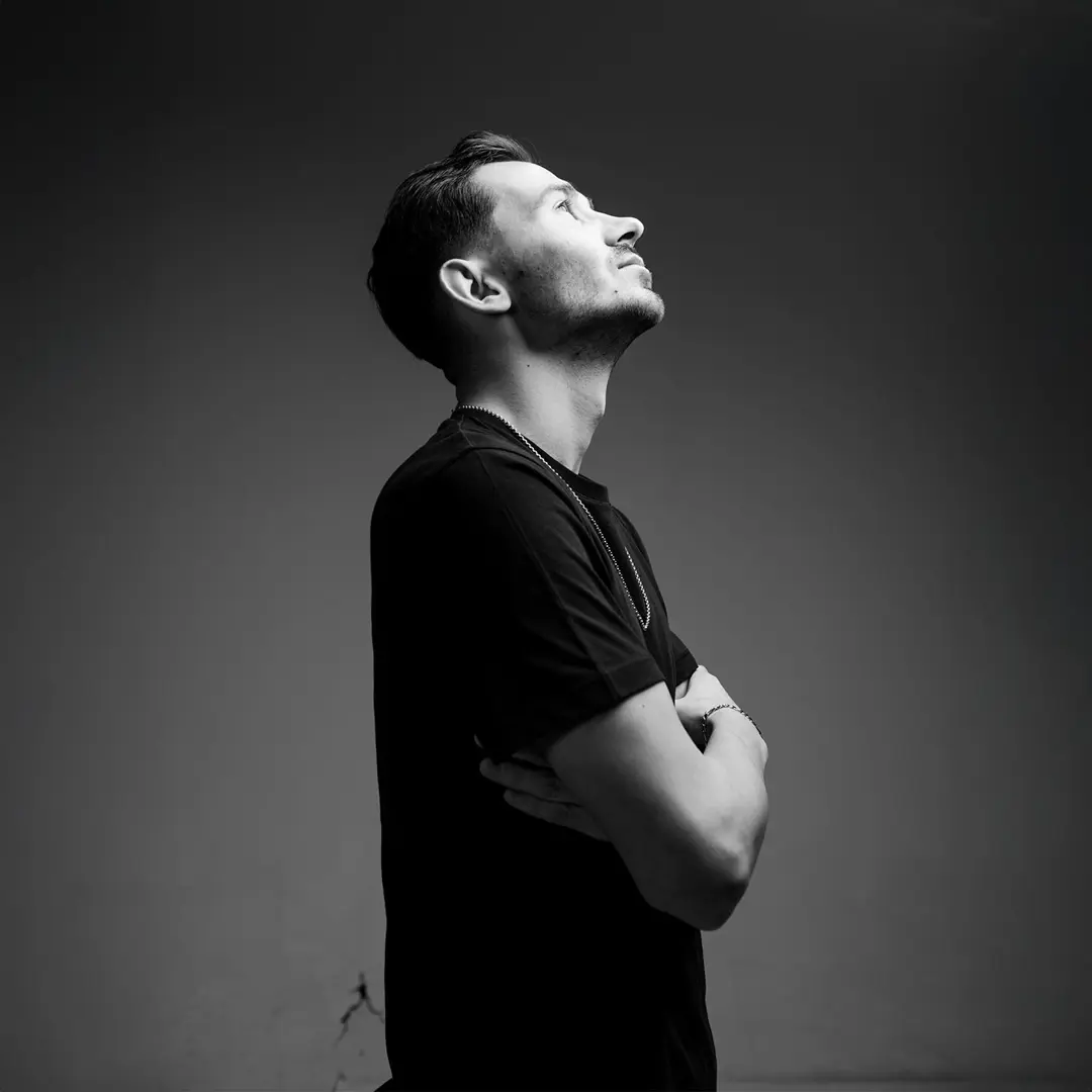 Siyah tişörtlü müzisyen tam boy portresi, kollar çapraz göğüste, sola ve yukarı bakış, gri arka plan — İzmir spotify albüm kapağı fotoğrafı