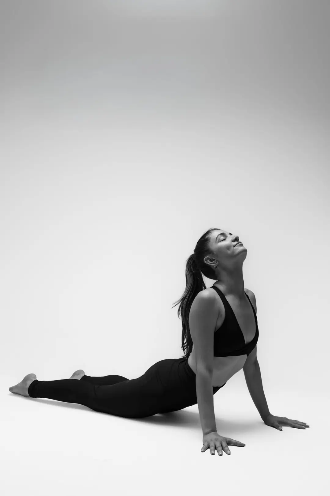 İzmir'deki stüdyoda gri fon önünde siyah kıyafetiyle asana duruşu yapan yoga eğitmeni yogawithmelis esnekliğini sergiliyor.