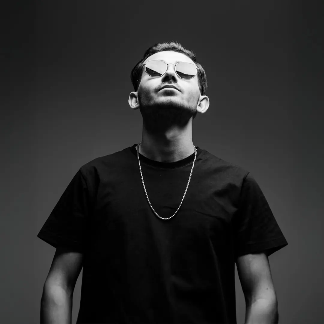 Siyah tişörtlü müzisyen güneş gözlüklü tam boy portresi, yukarı bakış, koyu gri arka plan — İzmir spotify single cover fotoğrafı