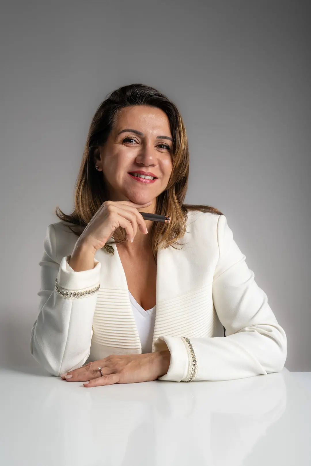 İzmir Dilara Karaçoban kurumsal portre fotoğraf çekimi açık fonda sağ elinde dolma kalemle masada tebessüm eden renkli portresi.
