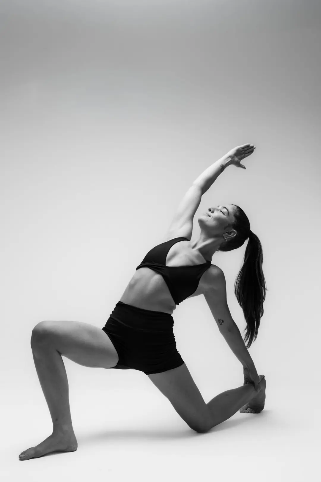 İzmir Menemen'deki stüdyoda gri fon önünde klasik bir asana duruşu sergileyen yoga eğitmeni Melis'in siyah beyaz yoga fotoğrafı.