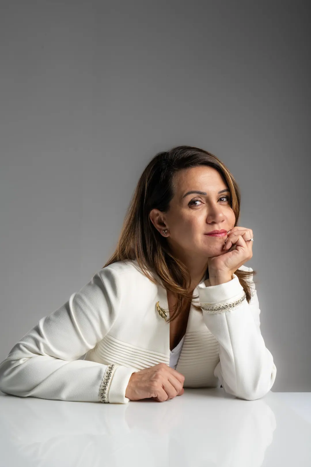 Dilara Karaçoban kişisel marka fotoğraf çekimi masada çenesini ellerine dayamış kadraj dışına bakan sakin renkli stüdyo karesi.