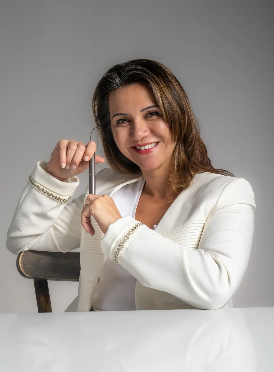 İzmir Dilara Karaçoban kurumsal portre fotoğraf çekimi açık fonda beyaz ceketle sandalyede dikey dolma kalem tutan renkli stüdyo portresi.