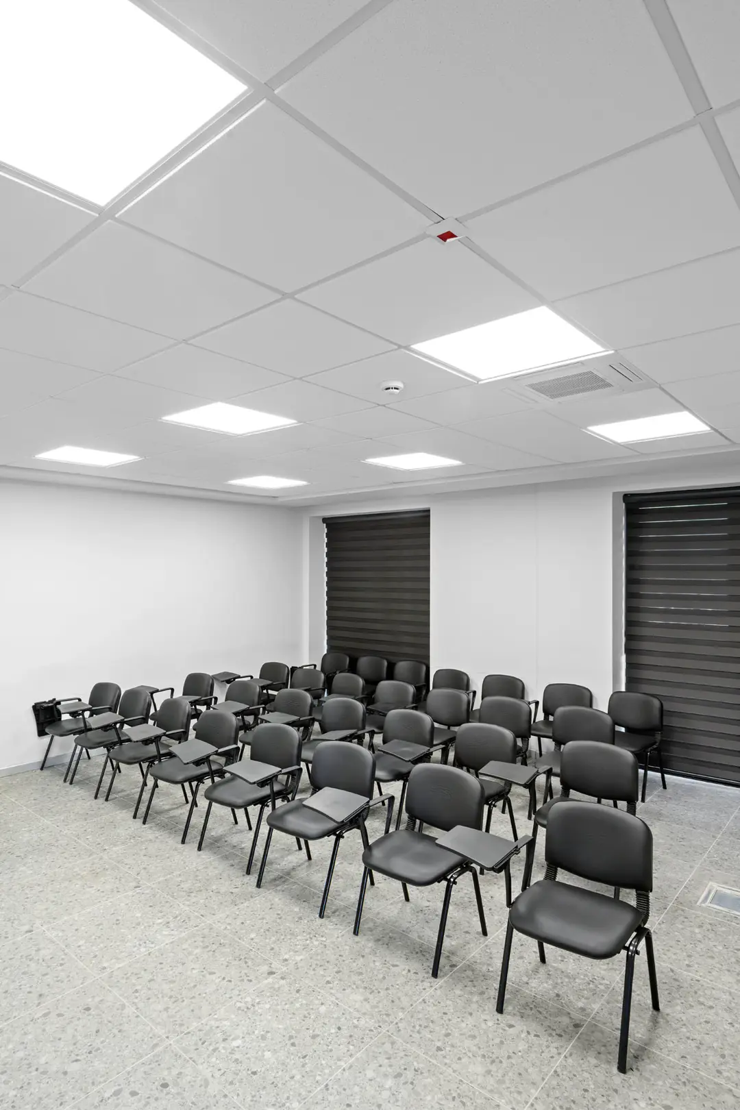İtfaiye eğitim salonunda modüler tavan ve LED paneller altında sandalye sıraları ve koyu zebra perdeler.