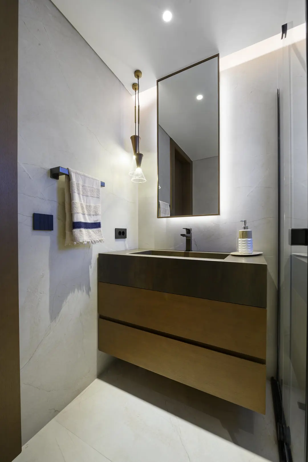 Dikey kadrajda banyonun ahşap lavabo ünitesi, arkadan aydınlatmalı ayna ve spot ışıkları, villa iç mekân fotoğrafı.
