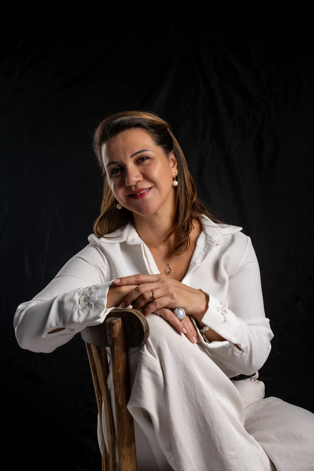Dilara Karaçoban kişisel marka fotoğraf çekimi stüdyoda ters ahşap sandalyeye kollarını kavuşturup tebessüm eden renkli portresi.