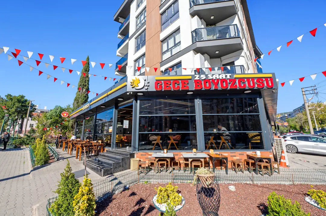 24 Saat Gece Boyozcusu dış cephesi, camlı salon, terası ve bayraklarıyla İzmir'de restoran mimari fotoğraf çekimi.