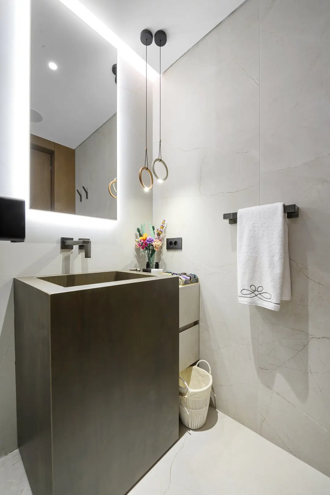 Banyoda koyu ahşap lavabo dolabı, aydınlatmalı ayna ve gri taş kaplama duvarlar, özel üretim banyo mobilyası.