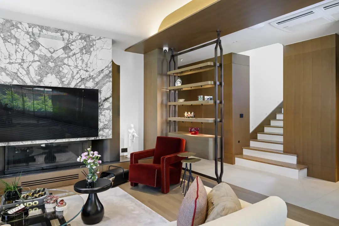 Özel villa salonunda mermer kaplı TV ünitesi, metal çerçeveli ahşap raflar ve kırmızı berjerler, geniş açı.