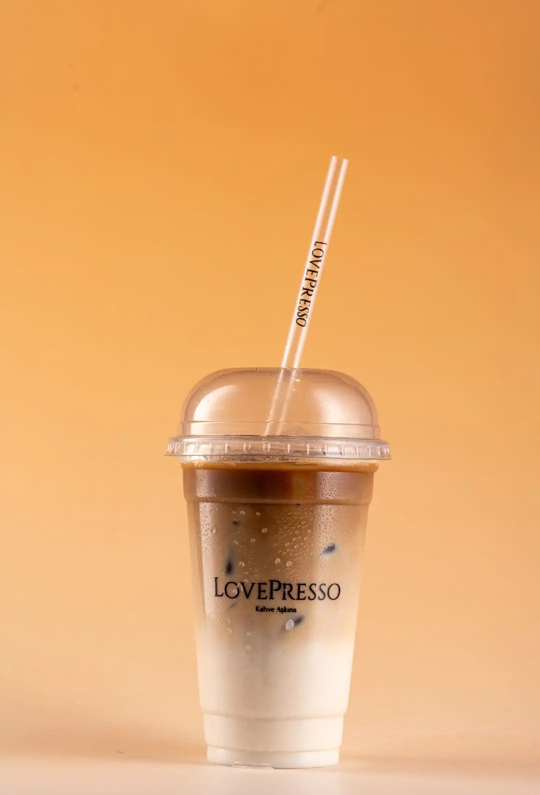 LovePresso iced latte kahve süt katmanlı, turuncu amber gradient PVC fon — İzmir dijital menü içecek fotoğrafı, Mert Akdurak