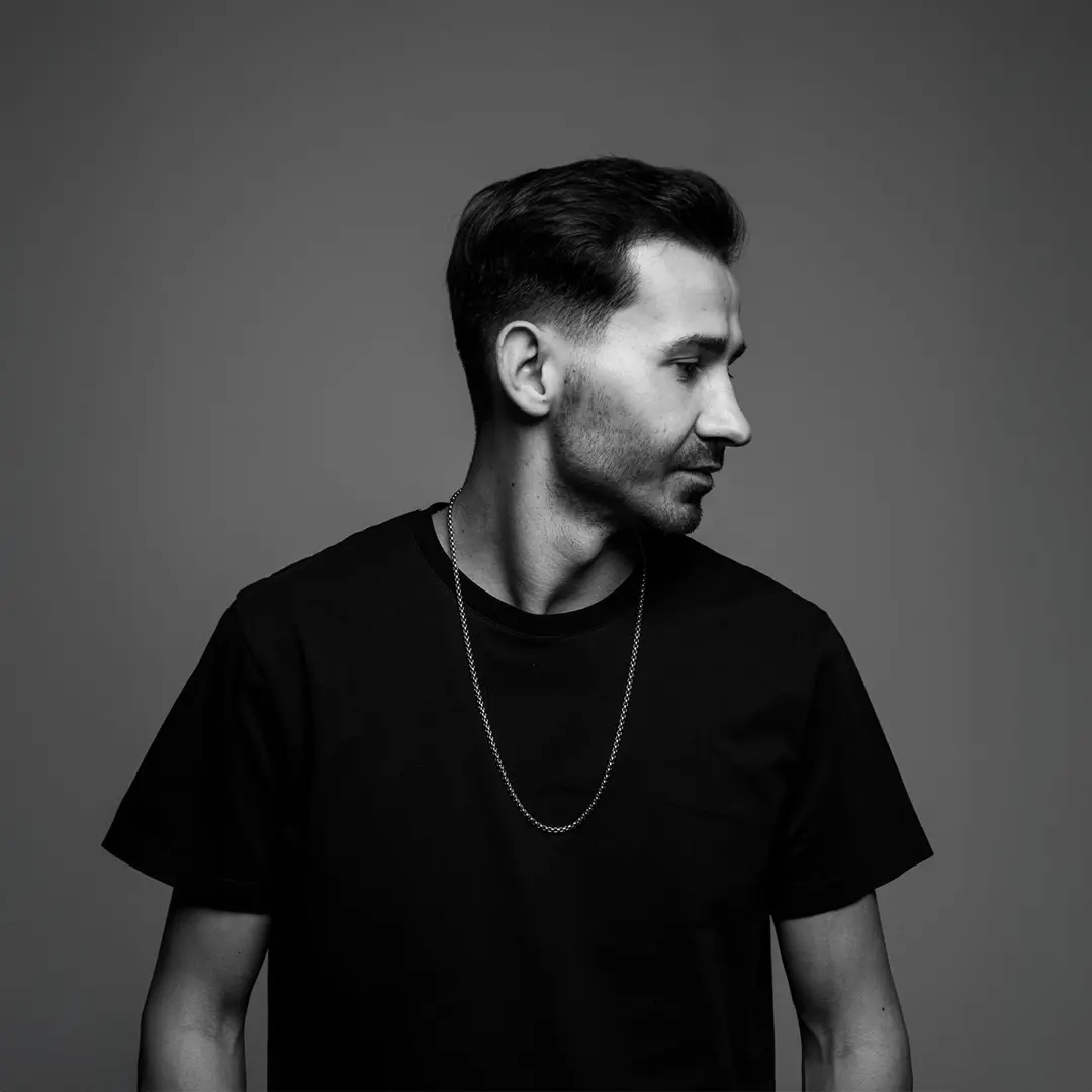 Siyah tişörtlü müzisyen yarım boy portresi, sola bakış, orta gri arka plan — İzmir spotify albüm kapağı fotoğrafı